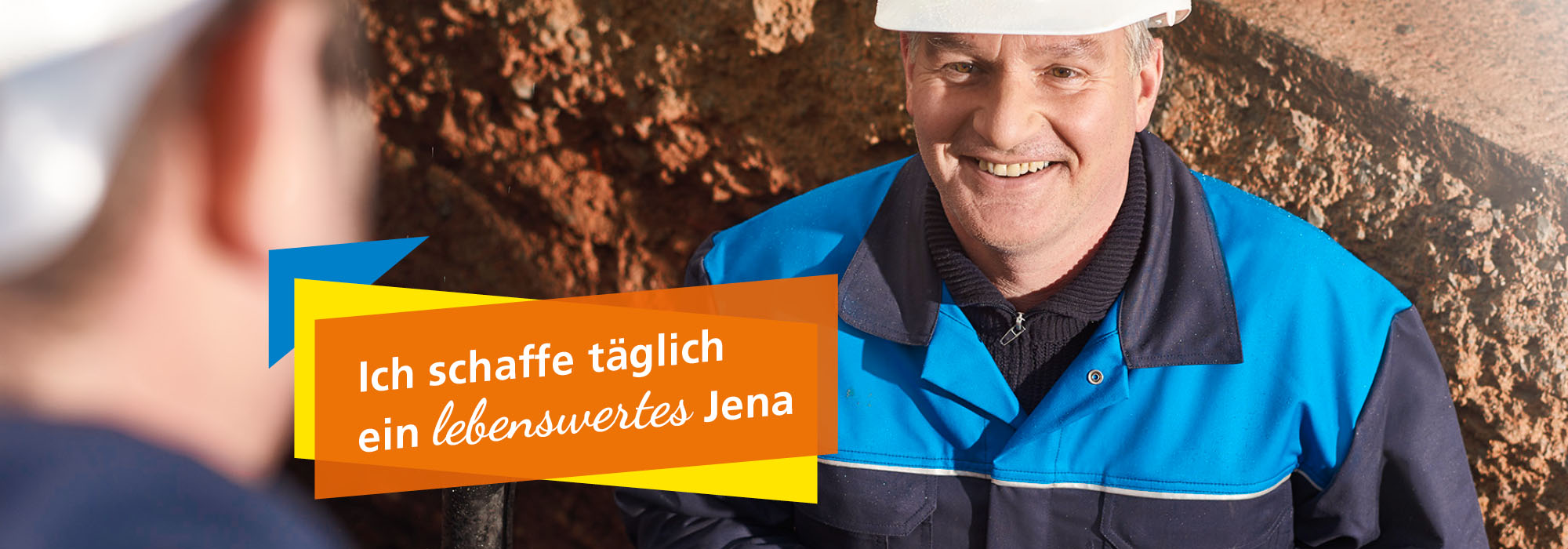 Ein Mann, der in Arbeitsbekleidung und Helm in einem Baugraben steht und sich einem Kollegen zuwendet. Daneben der Schriftzug: Ich schaffe täglich ein lebenswertes Jena.